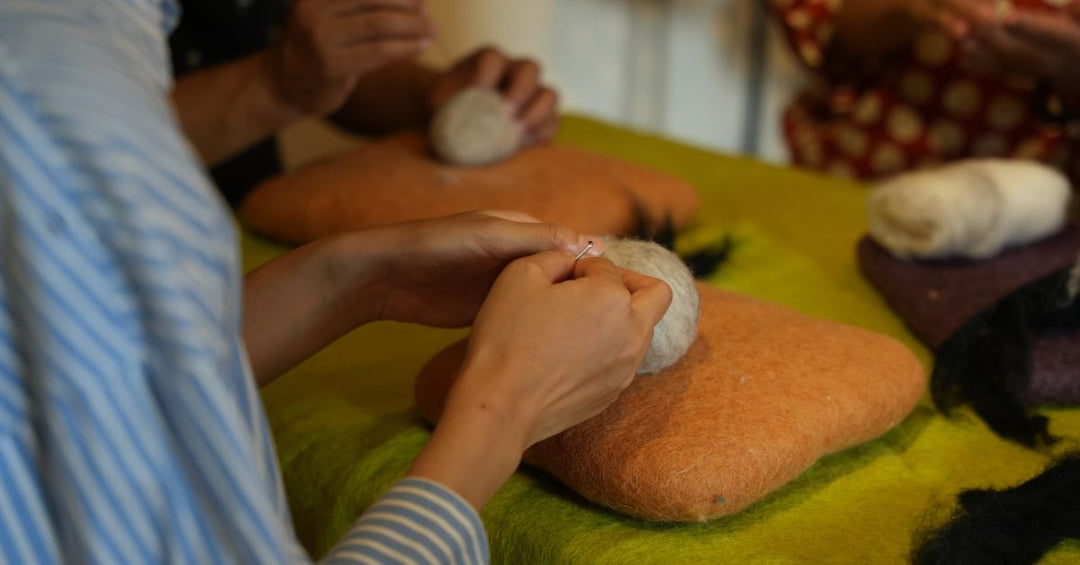 Woman needle felting a wool animal on a yellow wool mat in a sunlit room, symbolizing mindful making and creativity.